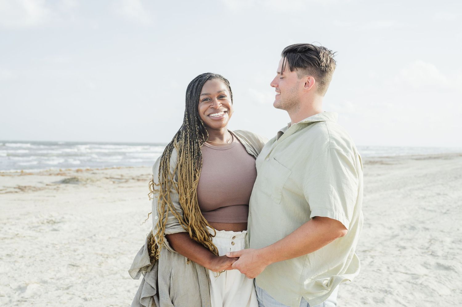 Couple walking along a beach shoreline at sunset while splashing in the waves and holding hands.