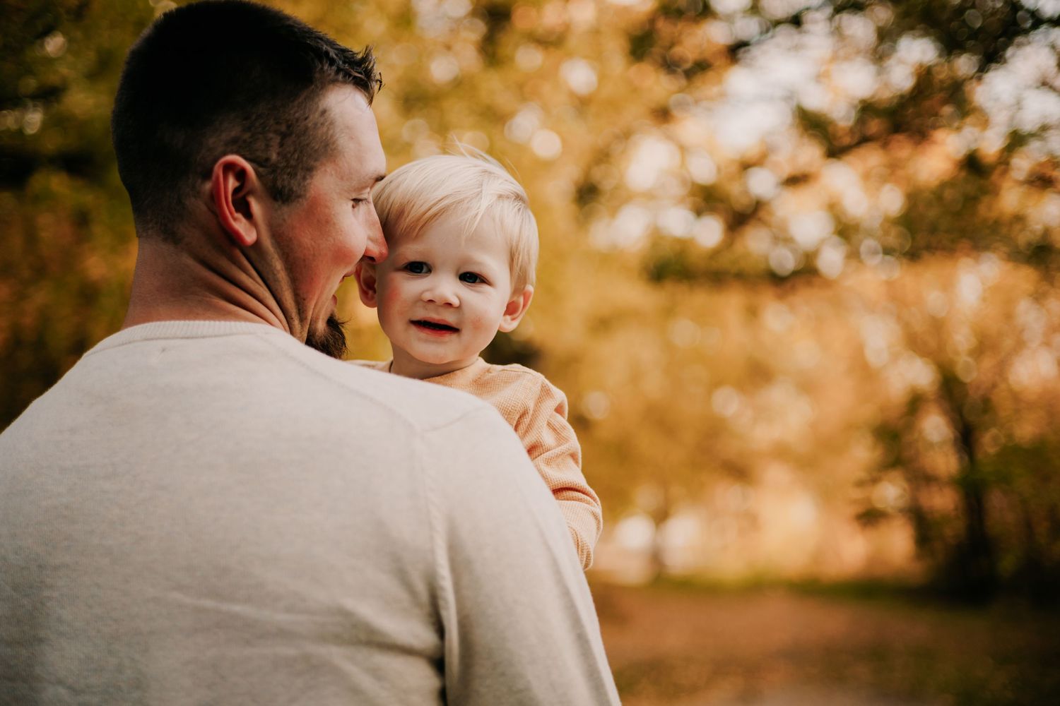 Parent holding smiling toddler outdoors during golden hour.