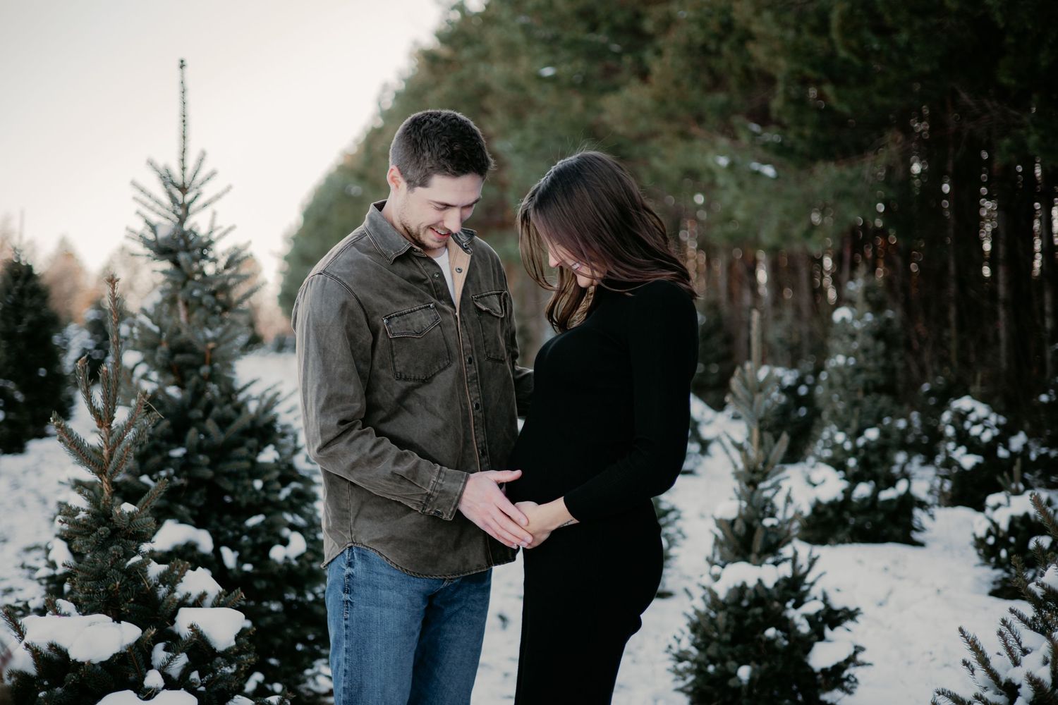 A couple shares an intimate moment among snow-covered evergreen trees.