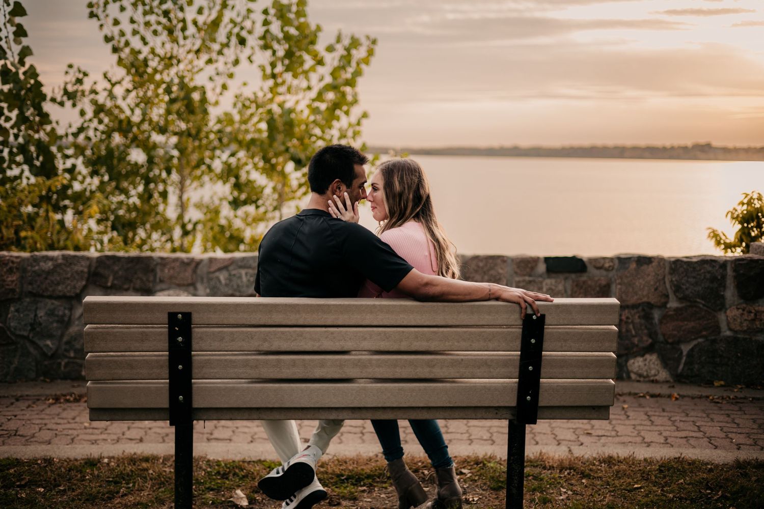 Couple sharing intimate moment on park bench at sunset overlooking water.