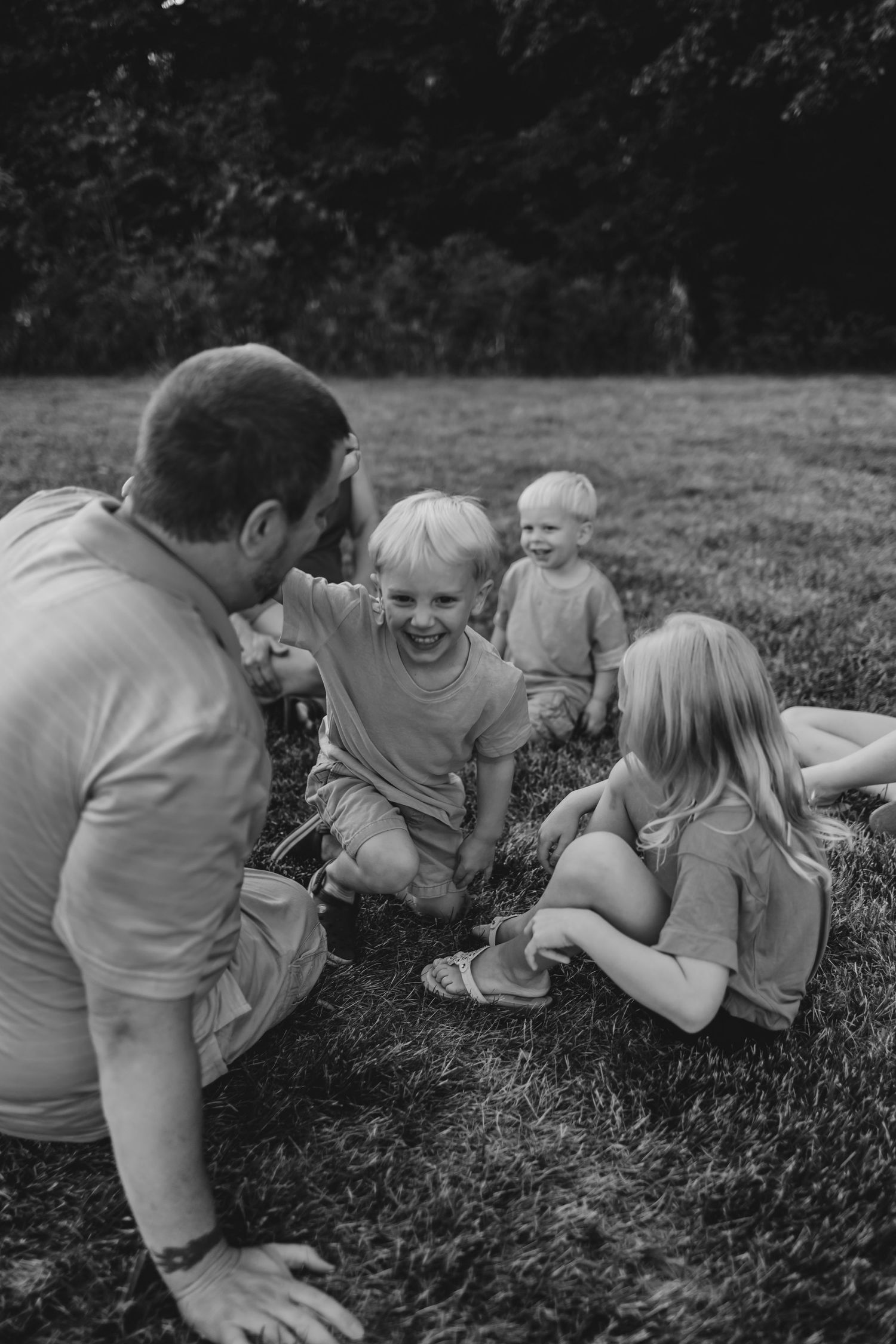 A candid black and white photo of a family enjoying a playful moment together on the grass.
