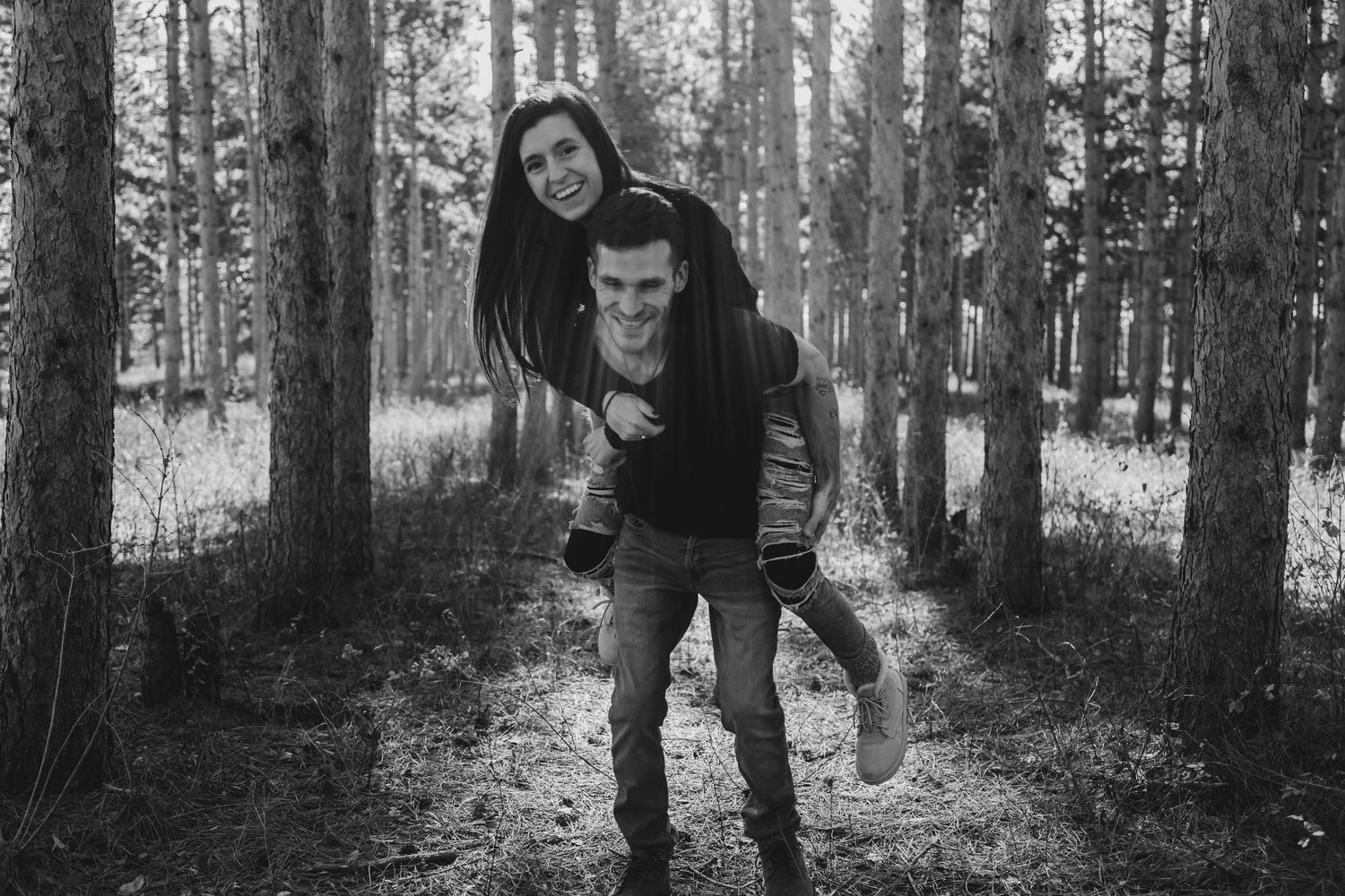 A playful piggyback ride moment captured in a forest setting with soft black and white tones.