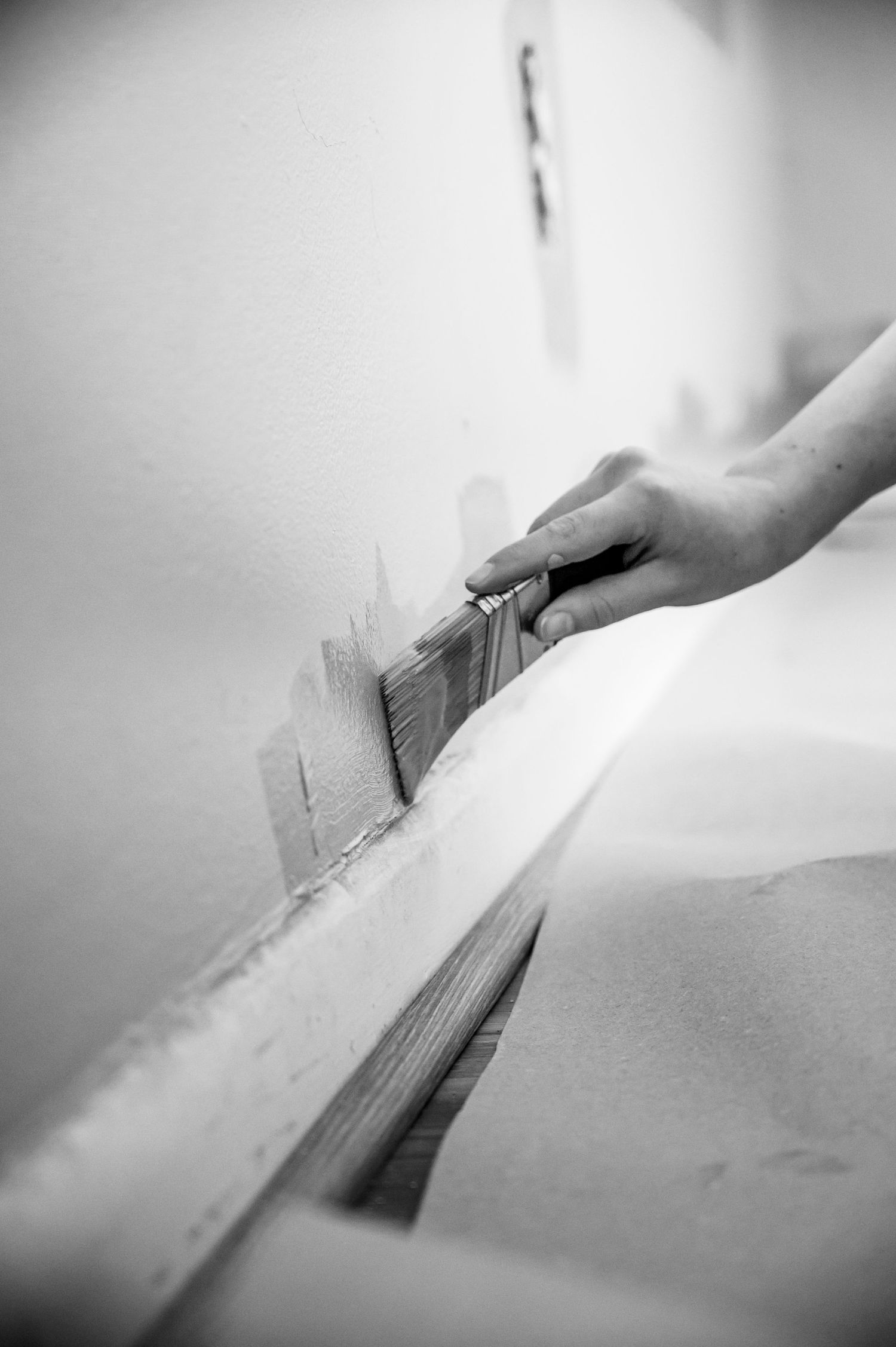 Close-up black and white shot of a hand using a putty knife to smooth a wall surface.