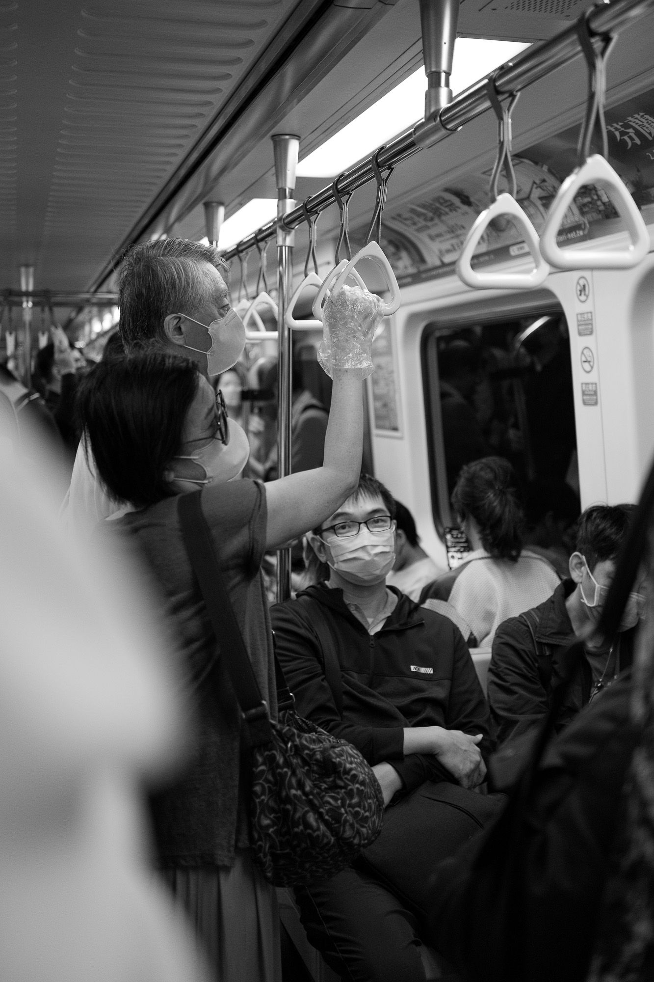 Black and white photo of a woman wearing plastic gloves and mask in the train, street photography.