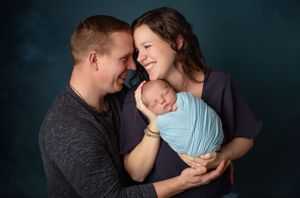 A tender family portrait with soft lighting and gentle expressions against a dark background.