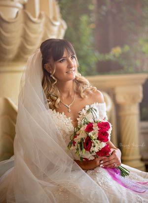 Bride with flowing veil holds red and white bouquet in elegant bridal portrait.
