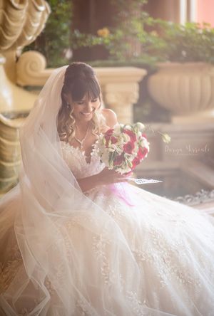 A bride in an elegant white gown holds a vibrant pink bouquet while sitting near decorative columns.