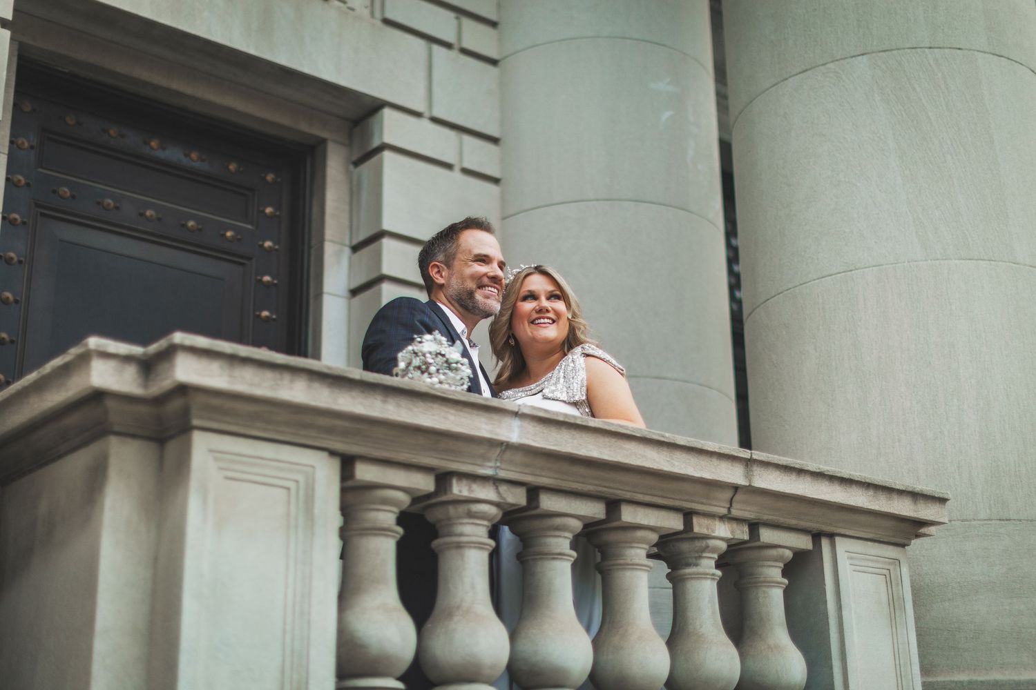A couple shares a joyful moment on a historic building's stone balcony.
