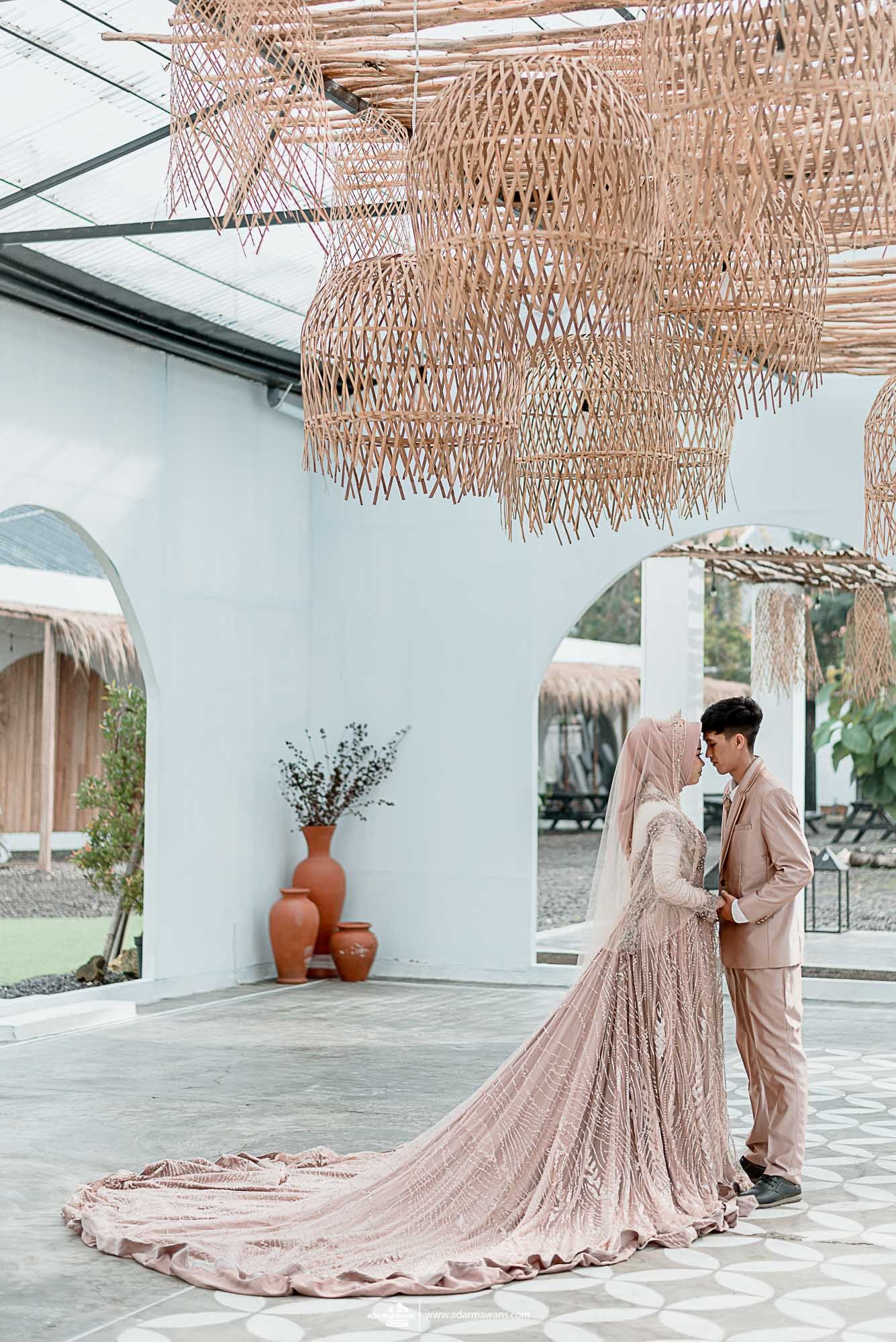 Wedding couple in blush attire under woven ceiling decorations with trailing dress.