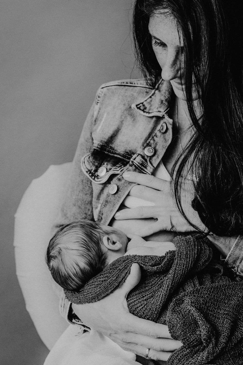Monochromes Bild zeigt intimen Stillmoment mit Baby in Strickdecke gewickelt.