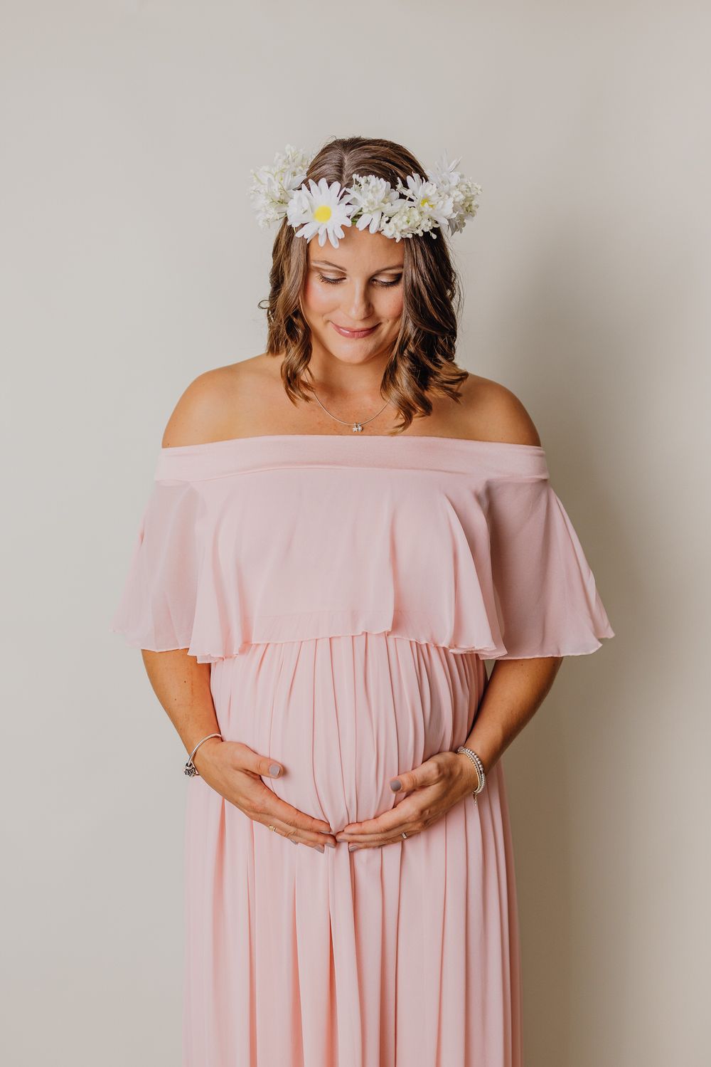 Frau in fließendem rosa schulterfreiem Kleid mit Gänseblümchenblumenkrone. Schwangerschaftsfoto