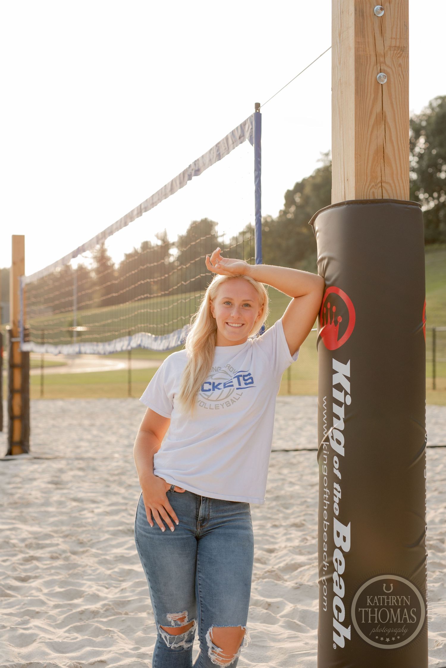 Athlete poses next to volleyball net post on sandy court at golden hour.
