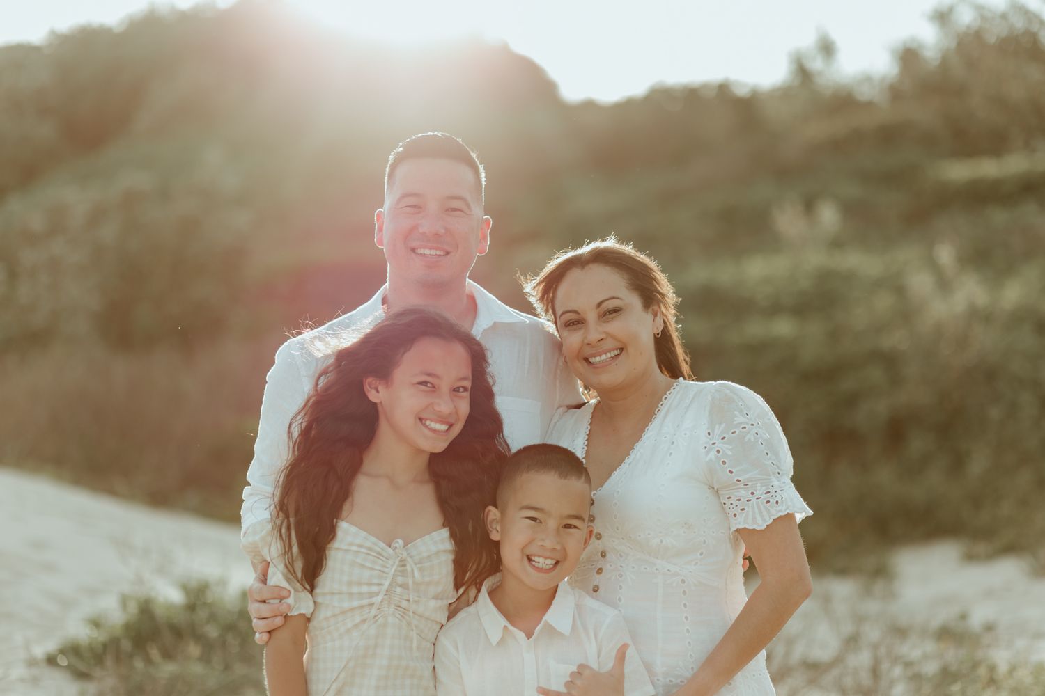 A family of four posing together for a portrait on a hillside at sunset.