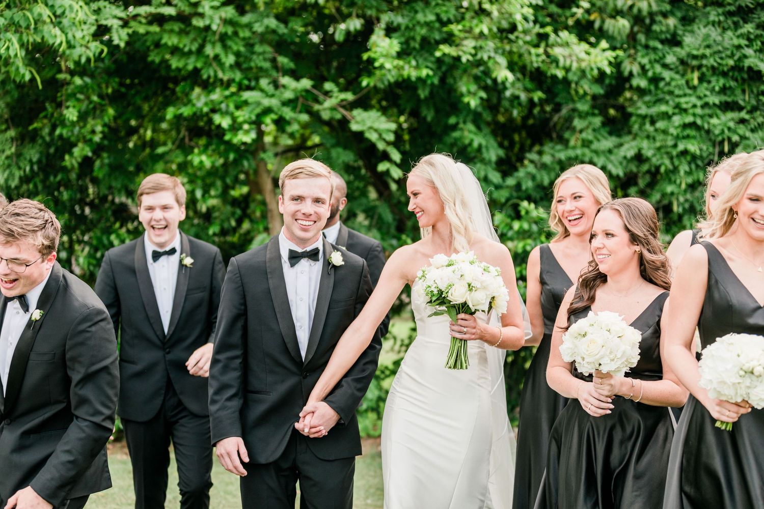 Wedding party laughs together outdoors during formal photo session.