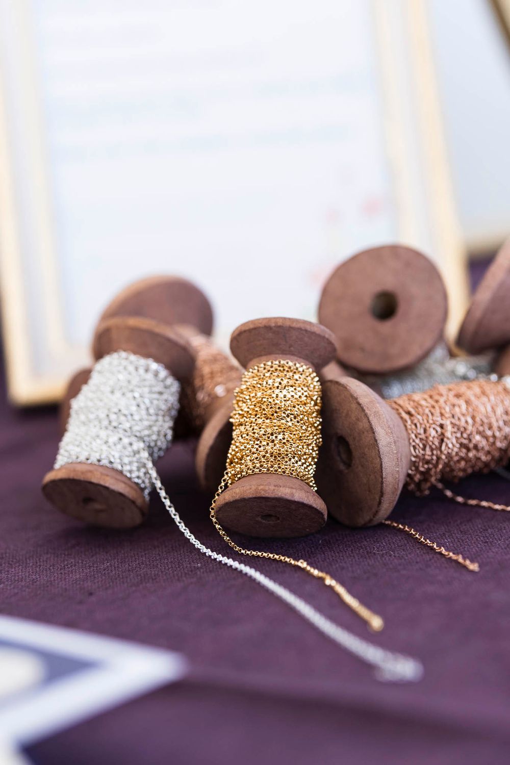 Vintage wooden spools with gold and silver chains wrapped around them on purple fabric.