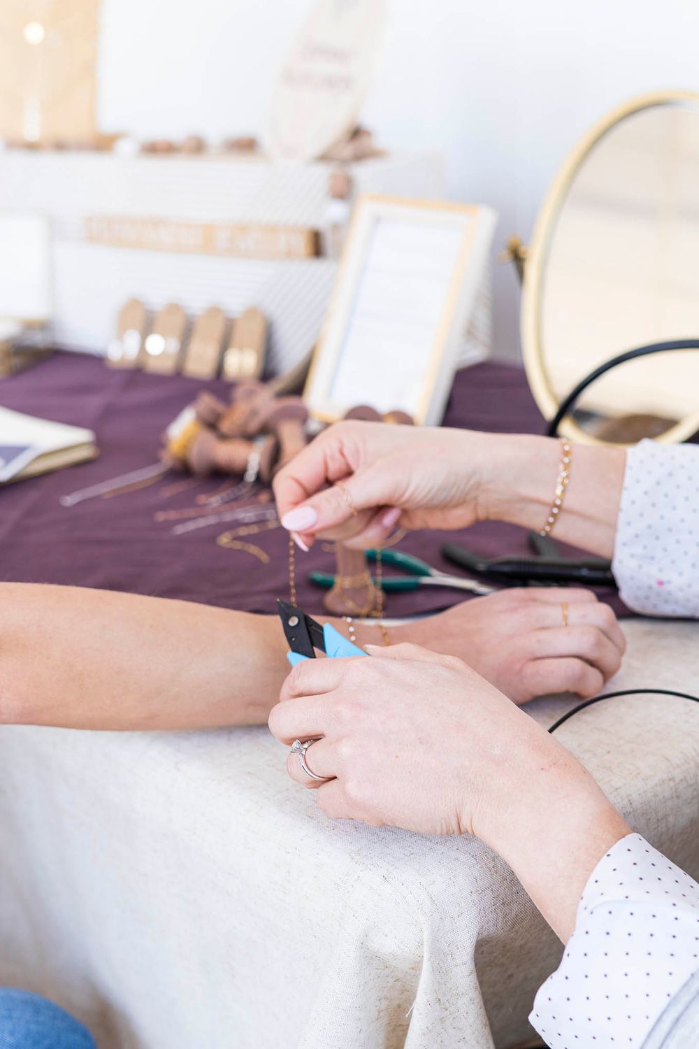 Hands working with jewelry tools and supplies on a purple workspace.