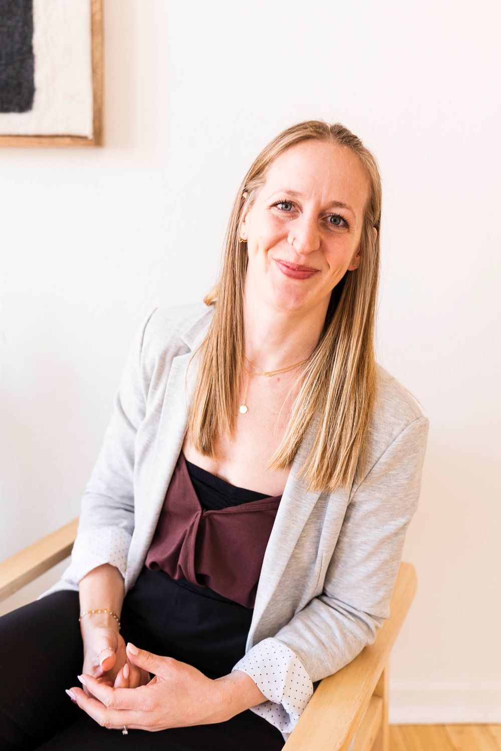 Person in business casual attire sitting in wooden chair against white wall.