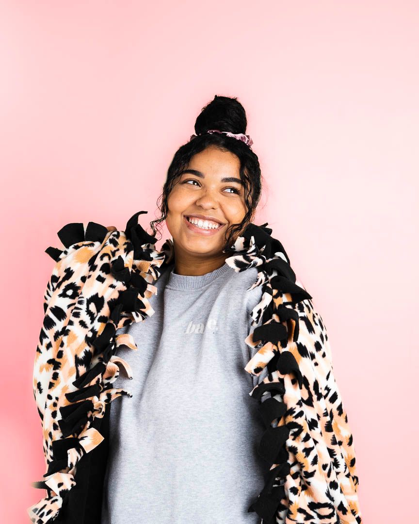 Person wearing a fun animal print coat and gray top smiling against a pink background.