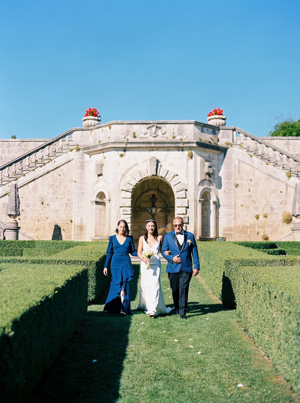 A bride with parents strolling through a formal garden during the bride's entrance at La Foce