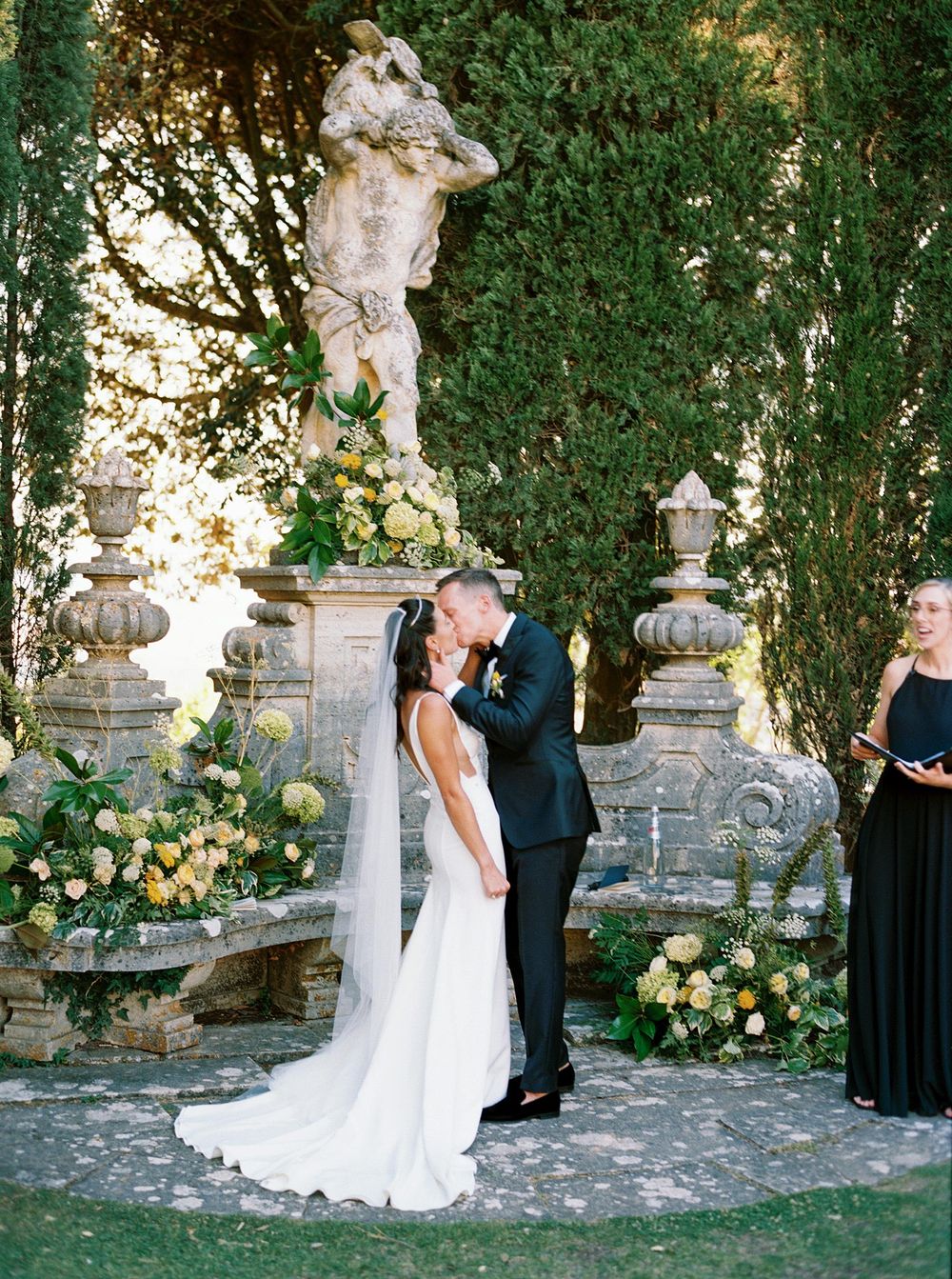 Bride and groom kissing during the wedding ceremony in the garden of La Foce, Tuscany.