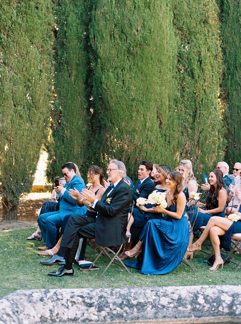 A wedding party in blue dresses sitting on chairs.