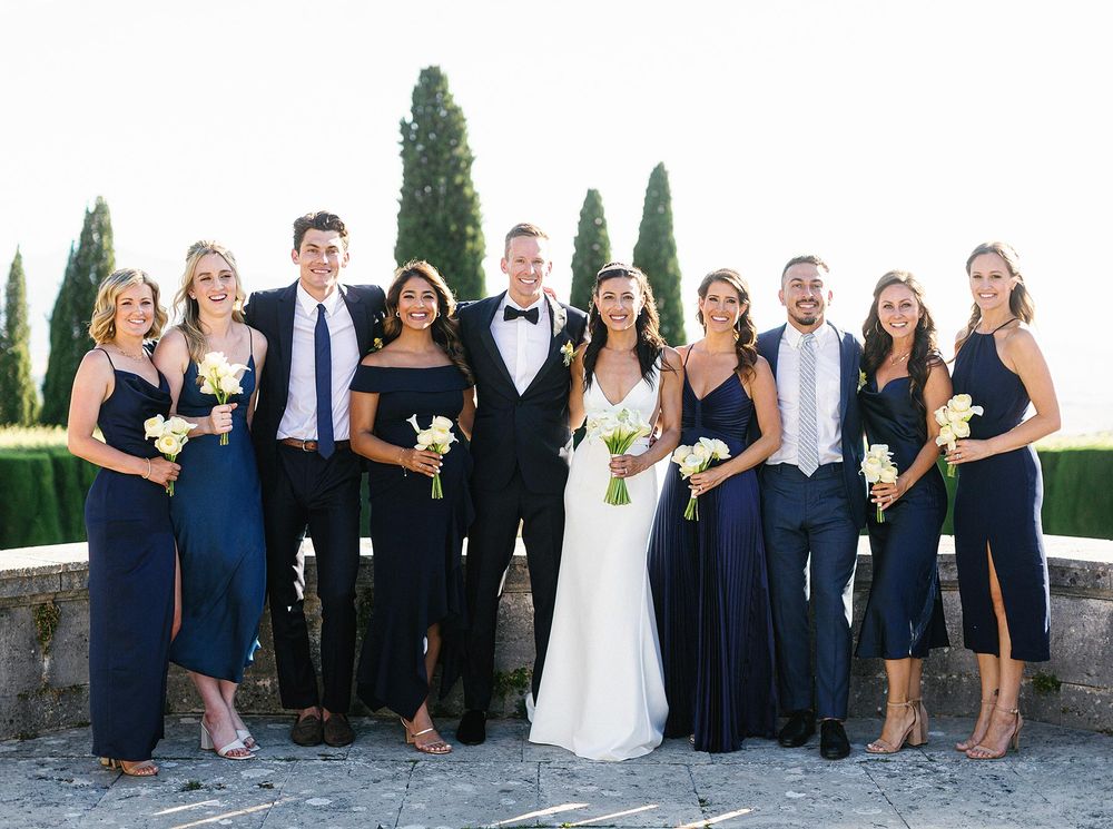 A wedding party in Tuscany, captured in a groupshot. Bridesmaids and groomsmen wearing navy blue dresses.