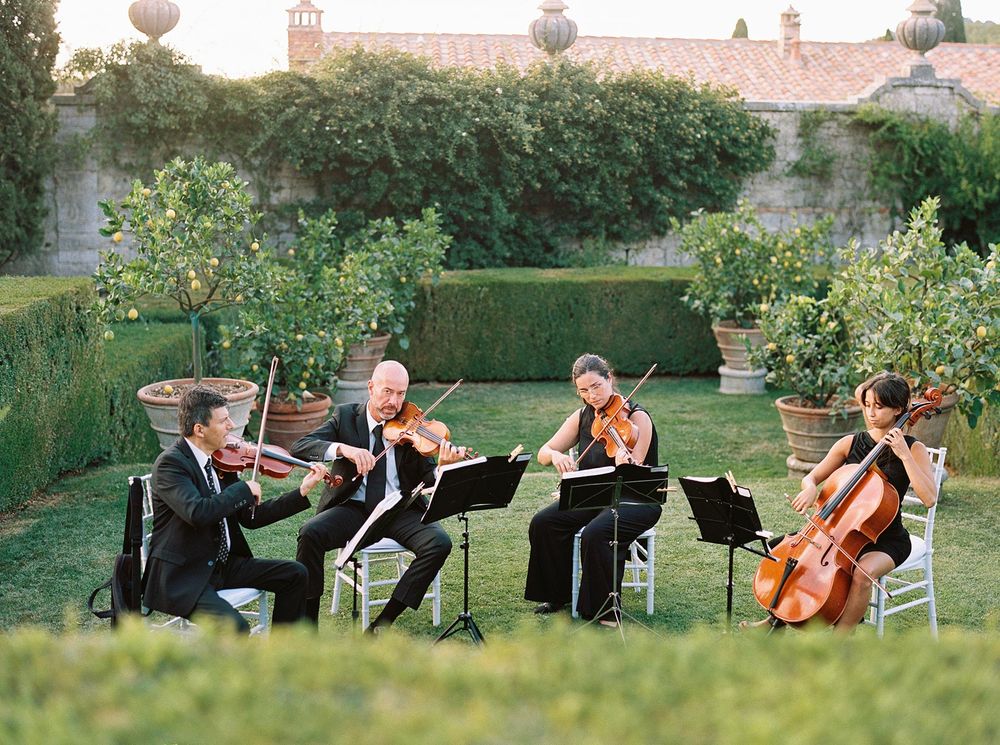 A group of musicians playing enchanting melodies amidst the serene beauty of La Foce, Tuscany's garden.