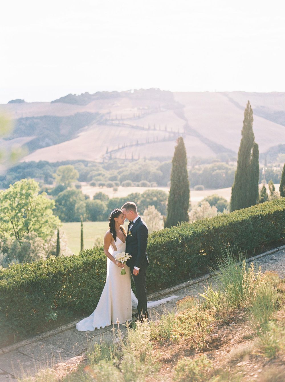 A beautiful bride and groom standing in the picturesque landscape of Tuscany, Italy.