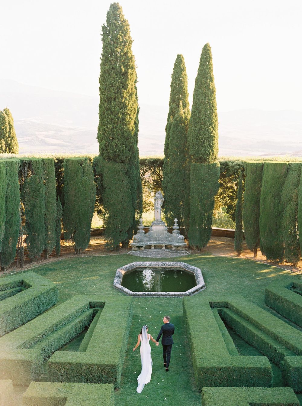 A wedding photographer capturing a beautiful moment of newlyweds in the garden of La Foce, Tuscany.