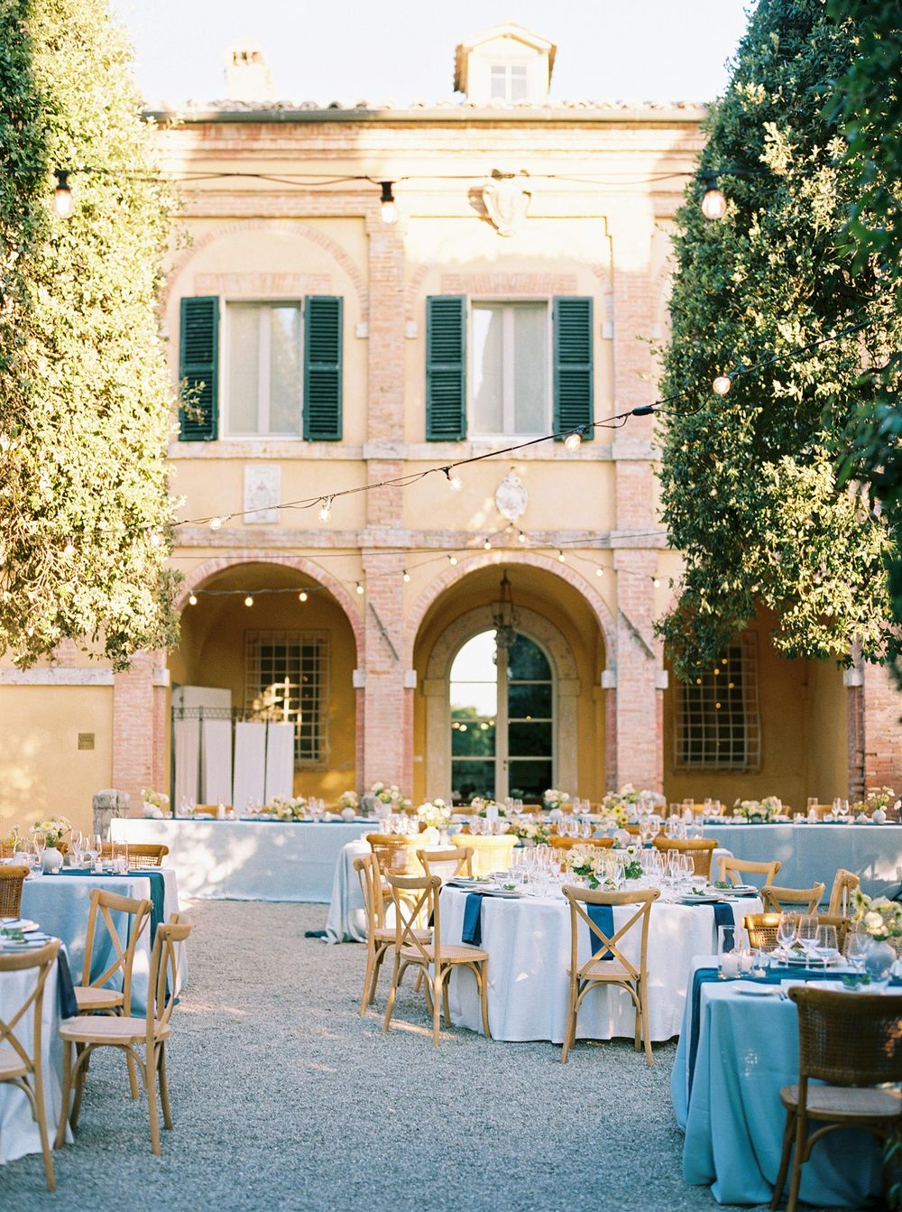 Wedding reception in a courtyard with tables and chairs in La Foce, Tuscany.