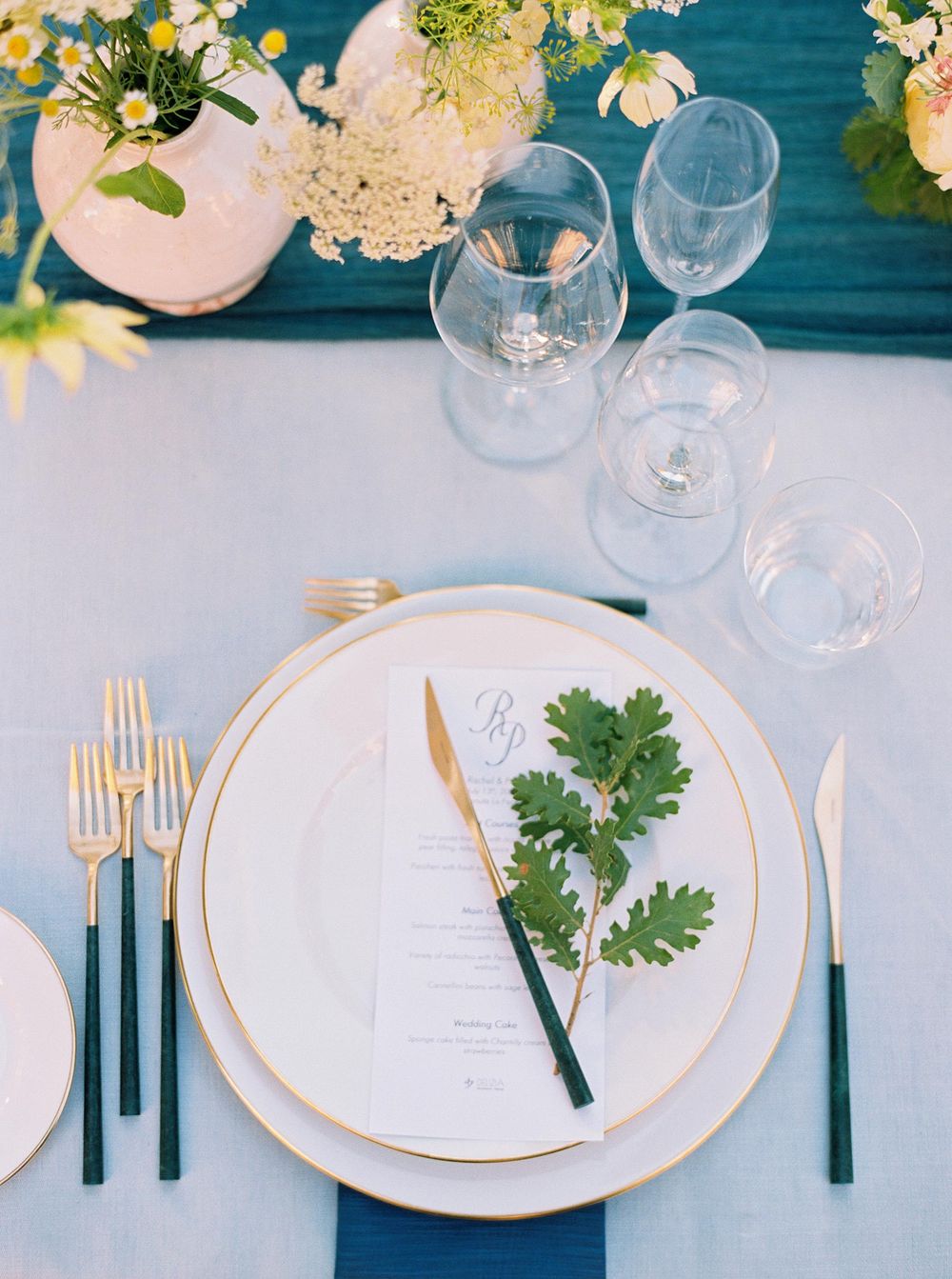 Wedding table with white tablecloth, elegant floral centerpiece, and gold-rimmed plates and cutlery.