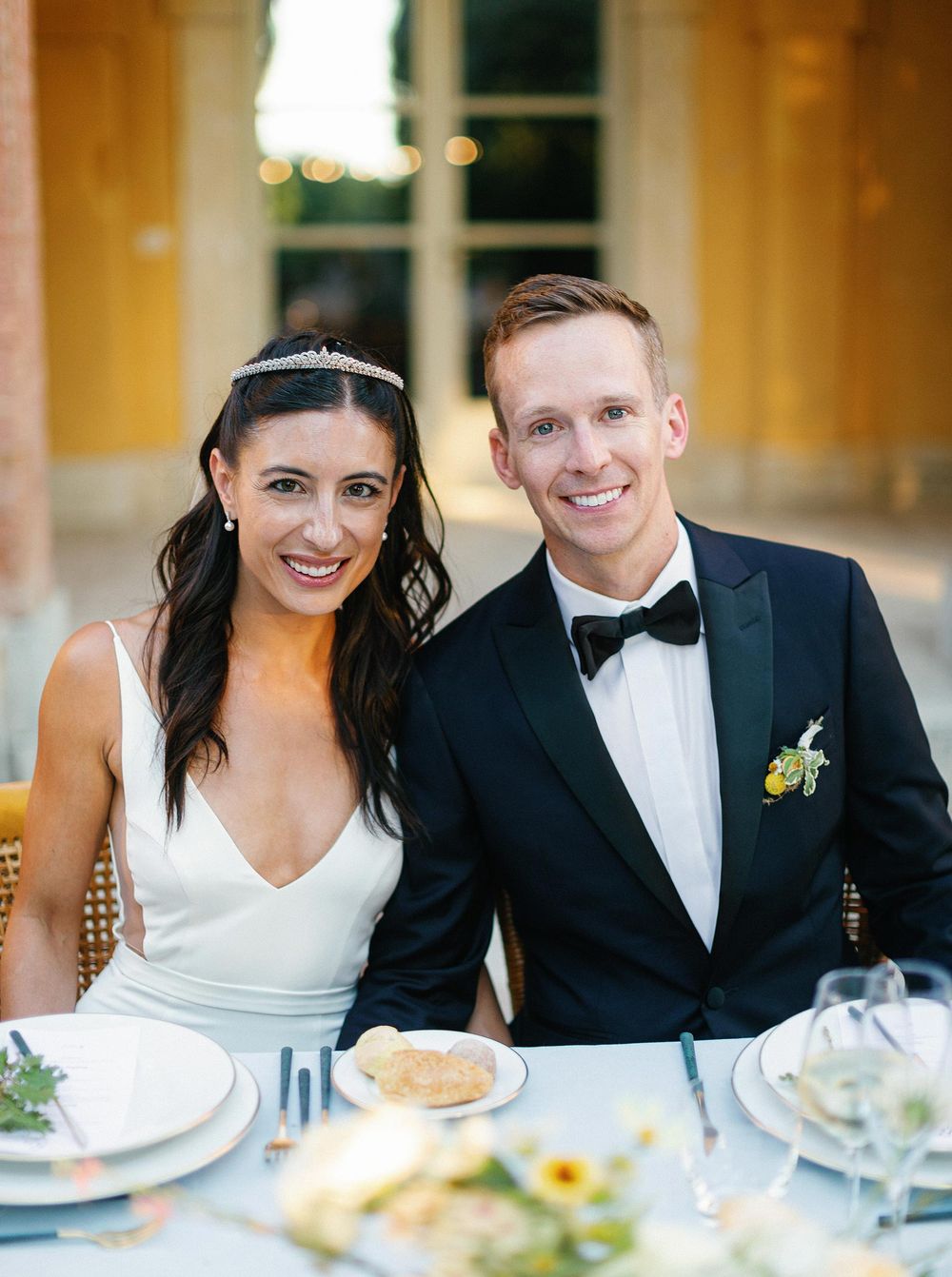 A newlywed couple seated at a beautifully decorated table, surrounded by vibrant flowers.