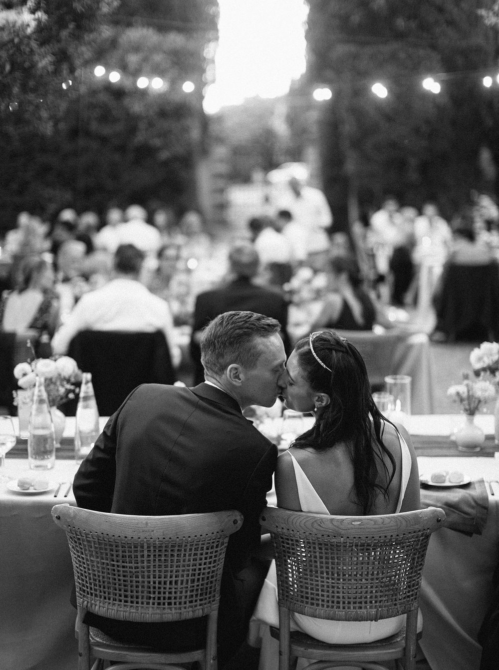 A bride and groom share a tender kiss at their wedding reception, standing by the wedding table.