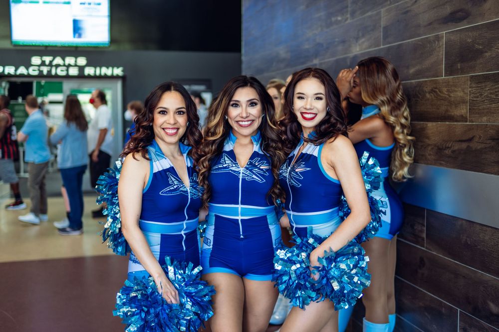 Cheerleaders in bright blue uniforms pose together at a sports venue.