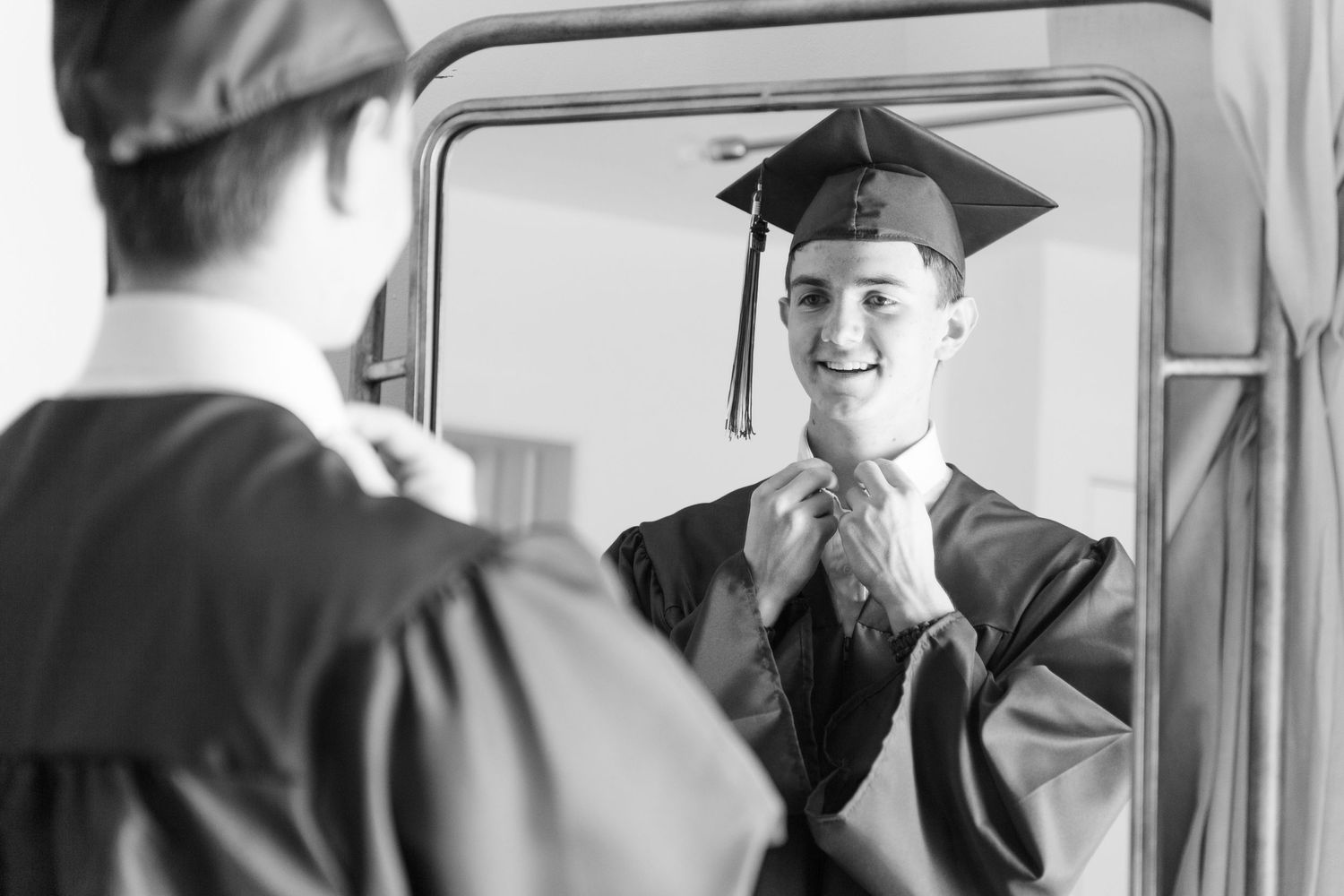 boy in graduation cap and gown smiling reflection in the mirror