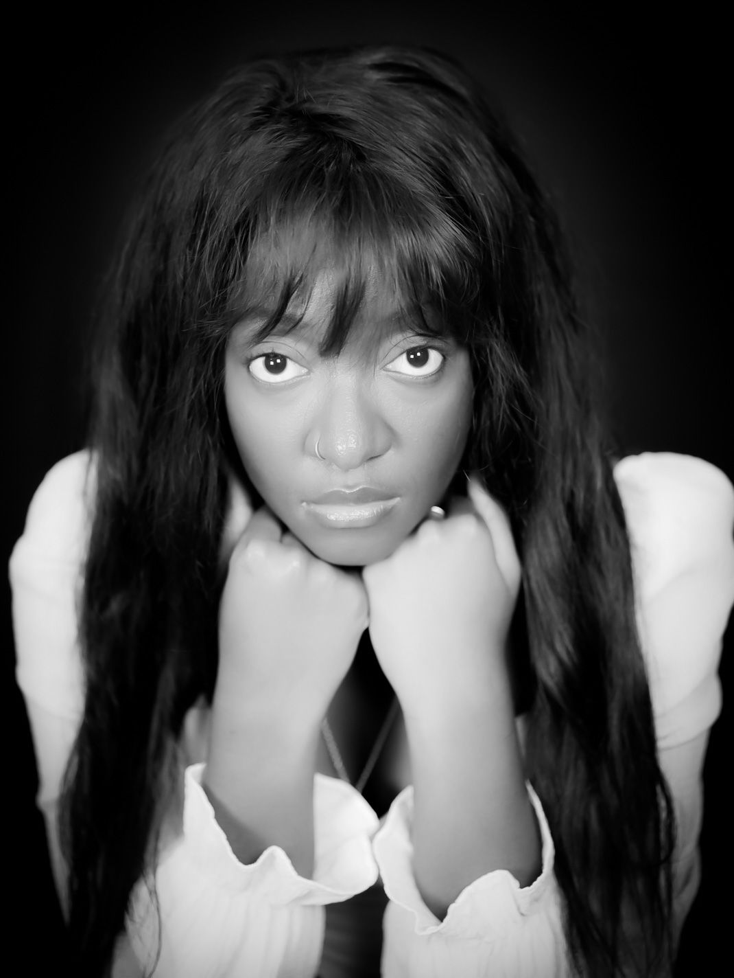 Black and white portrait of a young woman with long hair resting her chin on her hands.