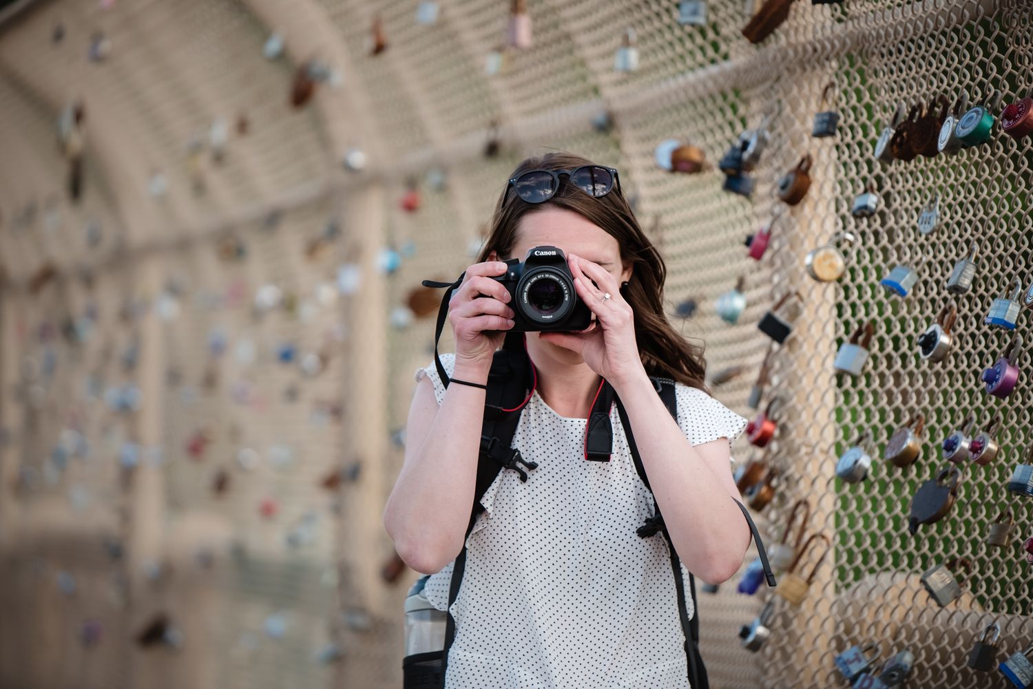 Young woman photographer taking photos with DSLR camera on bridge with padlocks.