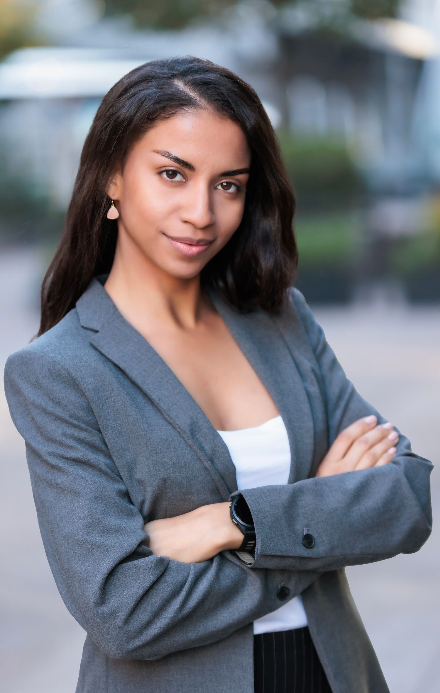 Professional in grey blazer and white top poses confidently outdoors.