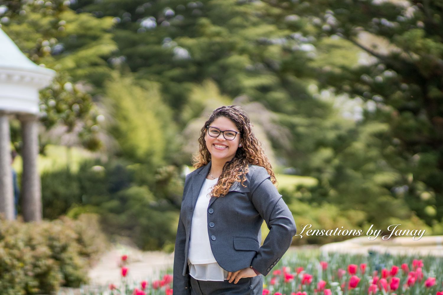 Professional woman in gray blazer smiling outdoors near colorful tulip garden.
