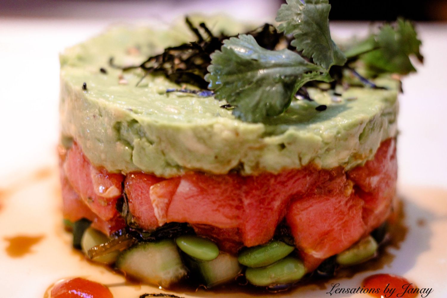 A gourmet tuna tartare layered with avocado and cucumber garnished with cilantro and sesame seeds.