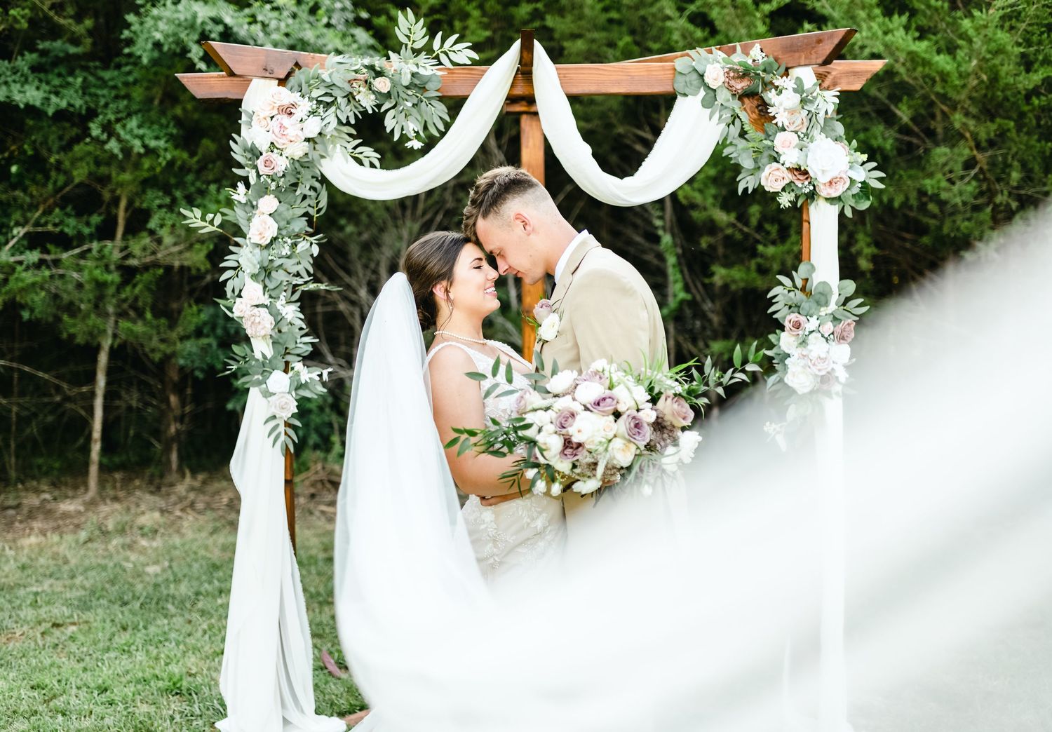 A wedding ceremony in a lush garden setting with white floral arches and decorative elements.