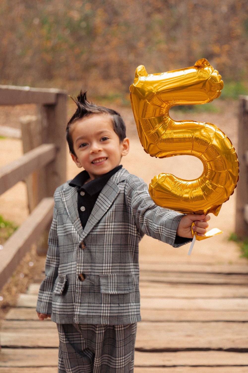 A cheerful moment captured with a gold number 5 balloon on a rustic wooden bridge.