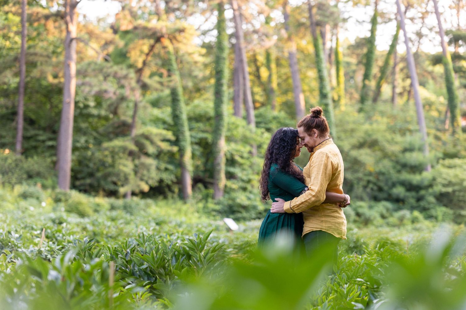 Couple embracing romantically in lush green forest ferns during engagement photo session.