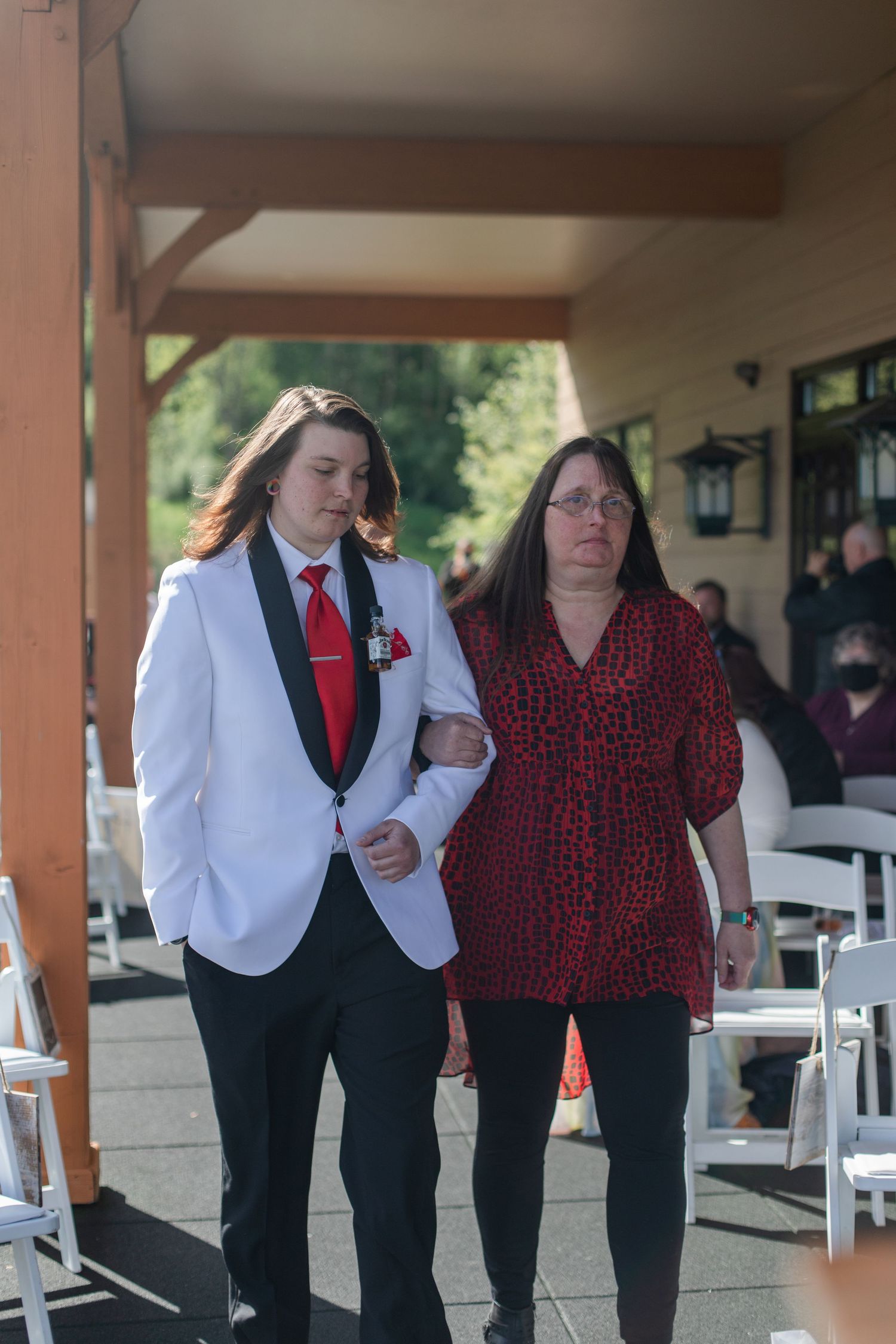 Wedding party members in formal attire walking under a covered outdoor venue.