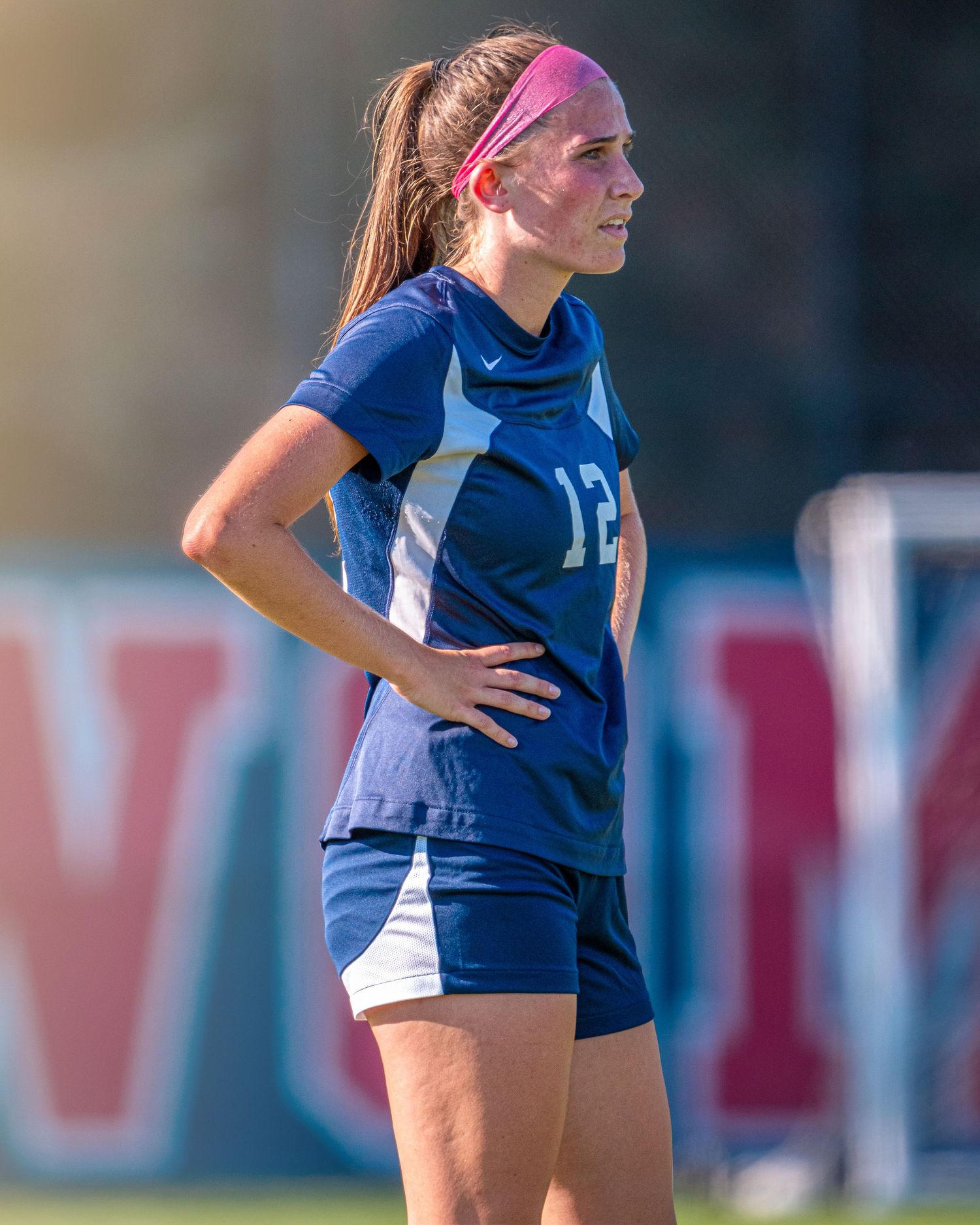 Soccer player in blue jersey stands with hands on hips during match.