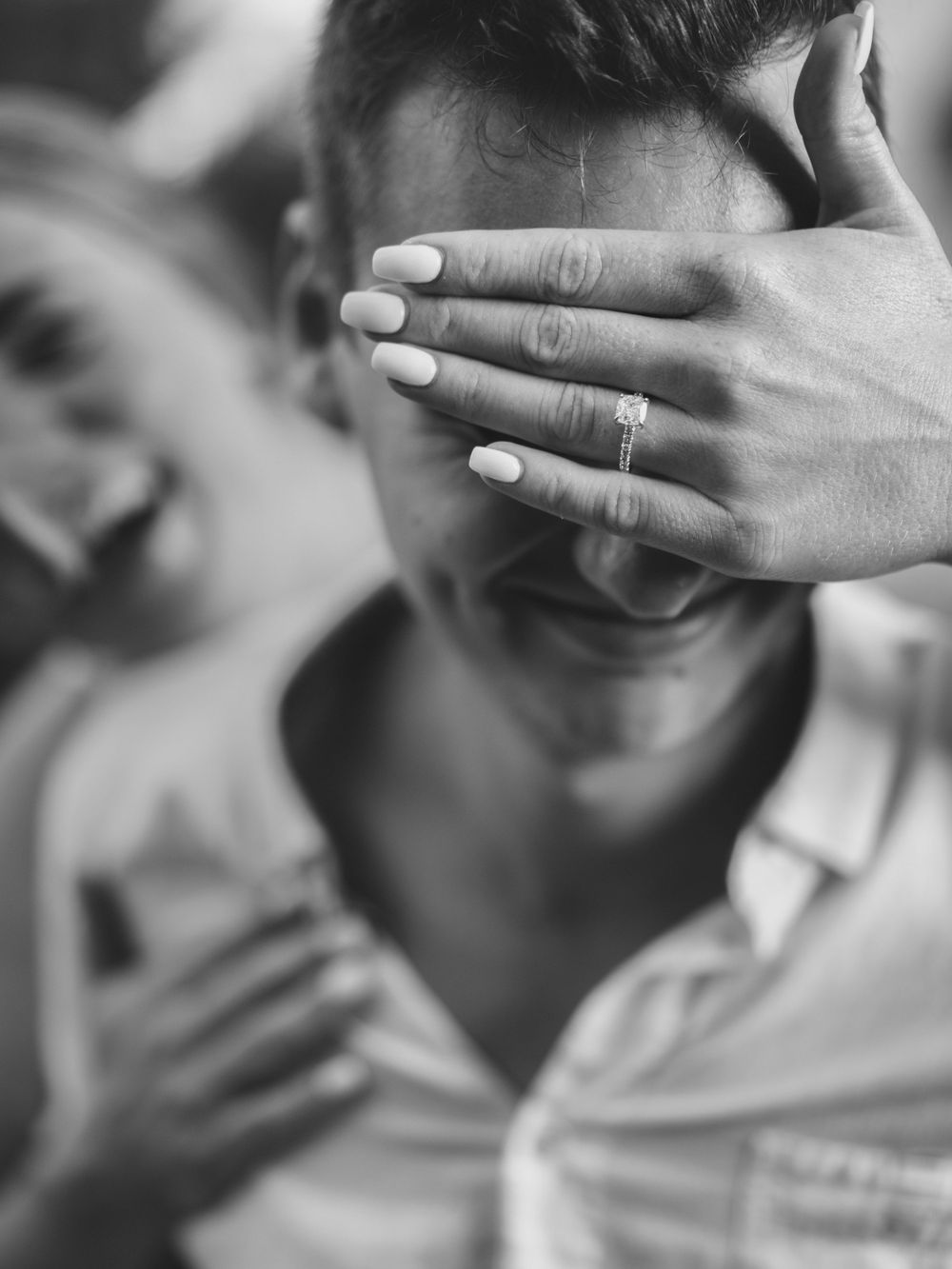 Black and white photo showing a hand with engagement ring covering a smiling expression.