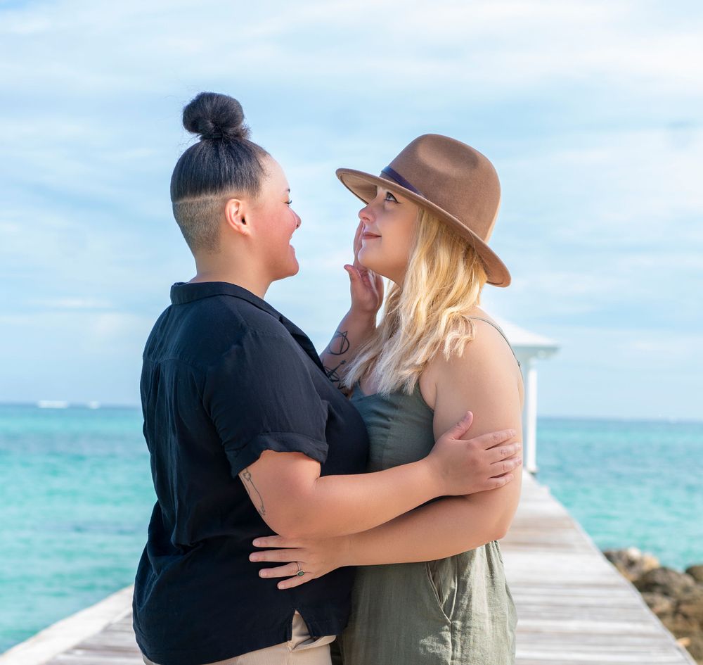 A couple sharing an intimate moment on a seaside pier with crystal blue waters behind them.