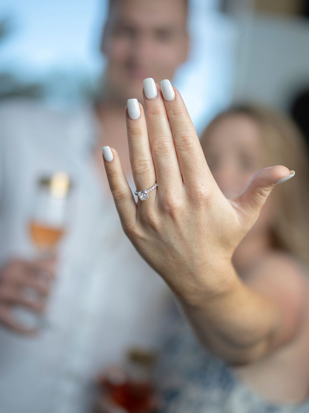 Close-up of a hand displaying an elegant engagement ring with white manicured nails.