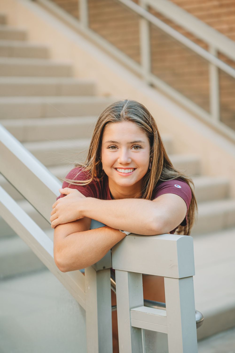 Student in maroon university shirt leaning on stair railing outdoors with natural lighting.
