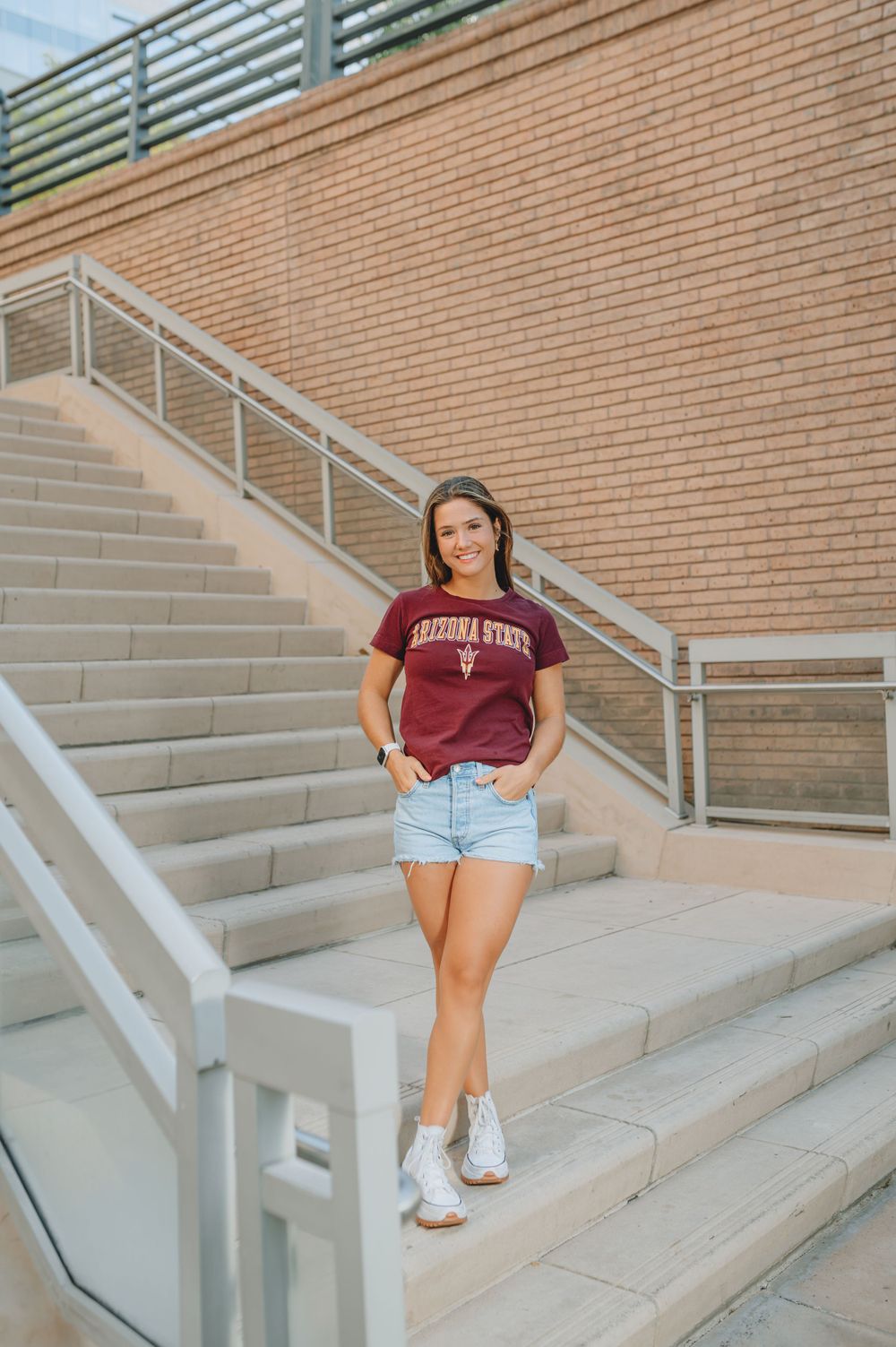 Person wearing Arizona State shirt and denim shorts standing on outdoor campus stairs.